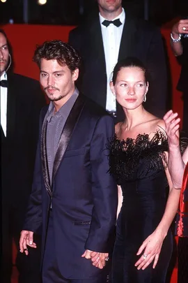 A man and woman in formal evening wear hold hands on a red carpet event.