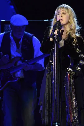 Fleetwood Mac performing on stage, with a lead female vocalist singing into a mic and a male guitarist in the background.