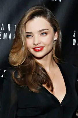 Miranda Kerr at a red carpet event, smiling, with long brown hair, wearing a black outfit.