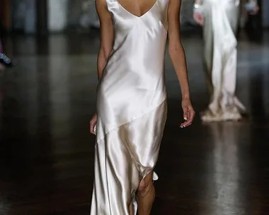 Model walking runway in a silver satin gown with beaded collar, showcasing elegant bridal fashion.