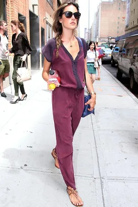 Woman in a burgundy outfit with braided hair and sunglasses, holding a drink on a city sidewalk.