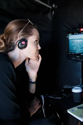 Angelina Jolie on the set of "Unbroken" wearing headphones, observing a screen with an ocean scene.