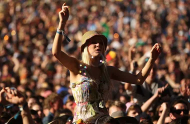 A woman enjoying a music festival, wearing a floral dress and hat, with a large crowd behind her.