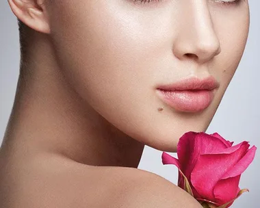 A woman with flawless skin holding a pink rose, gazing over her shoulder, promoting Lancôme skincare.