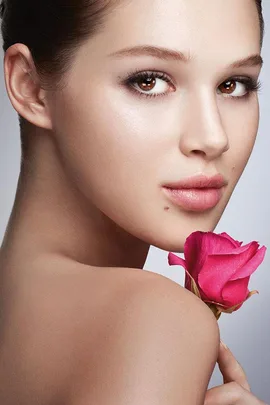 A woman with flawless skin holding a pink rose, gazing over her shoulder, promoting Lancôme skincare.