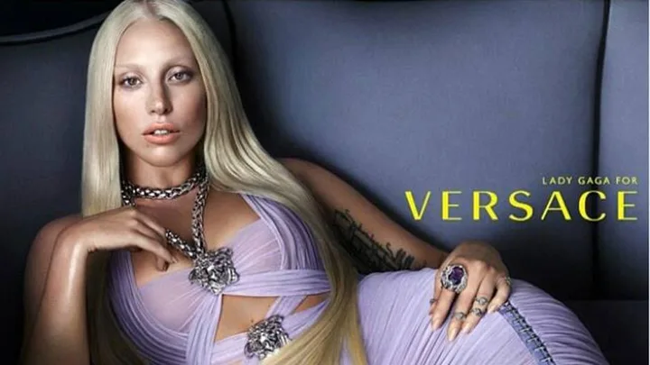 Lady Gaga in Versace SS14 campaign, lying on a couch in a lavender gown with platinum blond hair and bold jewelry.