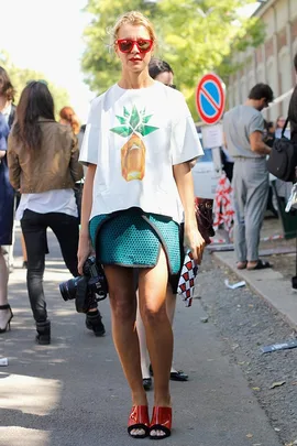 Woman in pineapple top with red sunglasses and camera, standing stylishly on a street.