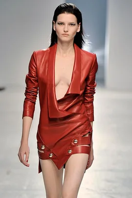 Model in a red, leather dress with plunging neckline walks runway in a fashion show.