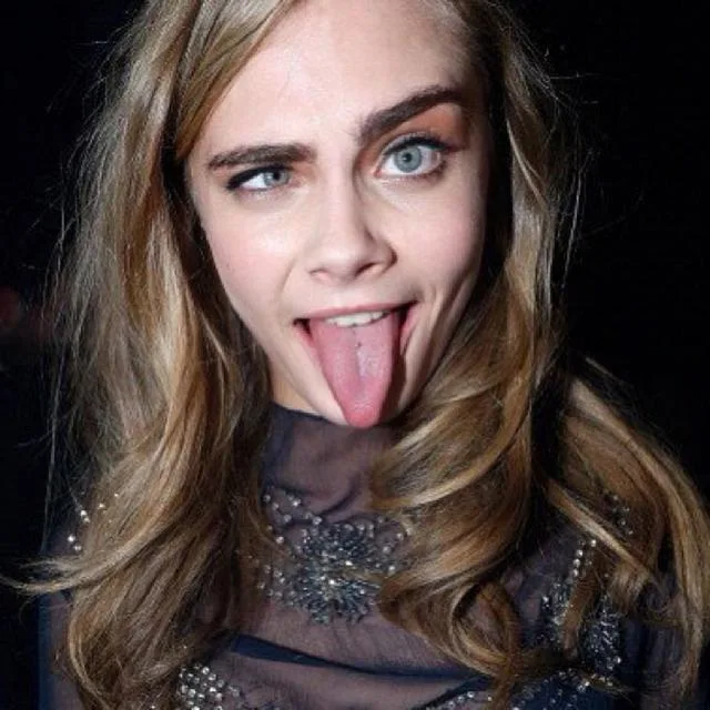 Model making a funny face with eyes crossed and tongue out, wearing a dark, embellished top.