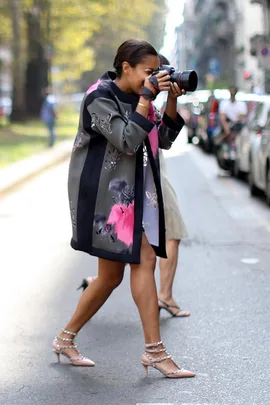 Photographer in floral coat and heels taking a picture on a city street during Milan Fashion Week SS14.