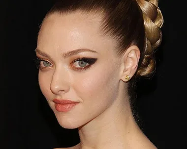 Amanda Seyfried with braided updo and gold dress at a formal event, posing against a black background.