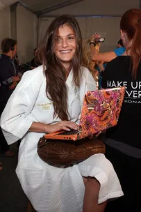 Woman smiling in white bathrobe holding colorful laptop, people in background.