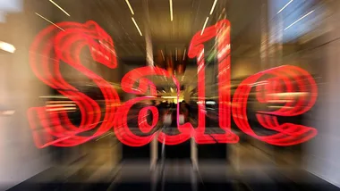 "Blurred red 'Sale' sign in front of a store entrance, conveying a sense of urgency or excitement."