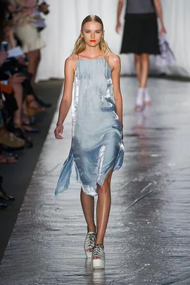 Model in a flowing silver dress and platform sneakers walks runway at fashion show.