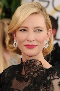 Actress with blonde hair and diamond earrings wearing a black lace dress.