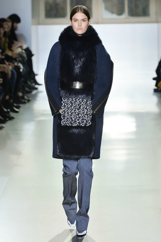 Model on runway wearing navy coat with fur trim, patterned detail, and tailored pants at Balenciaga Fall/Winter 2014-15.