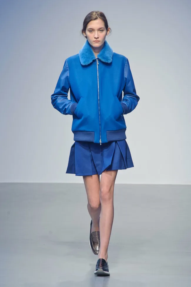 Model in blue jacket with fur collar and matching skirt, walking on runway during Richard Nicoll AW14-15 collection.