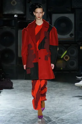 Model wearing a red and black geometric coat with matching red patterned pants on a runway.