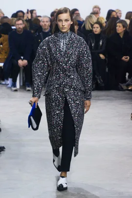 Model walking runway in floral coat and black pants, holding a clutch at Proenza Schouler AW 2014-2015 fashion show.