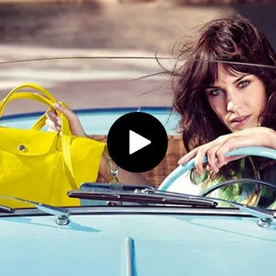 "Alexa Chung drives a vintage car while holding a bright yellow Longchamp handbag."