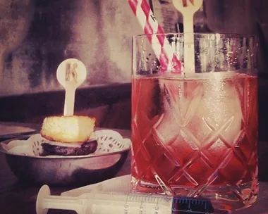 Elegant Bloody Mary cocktail with garnish in a glass, striped straw, and a small syringe on a napkin.