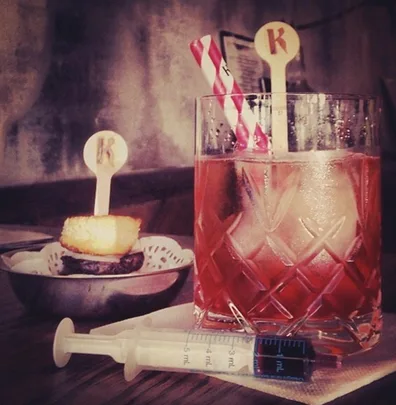 Elegant Bloody Mary cocktail with garnish in a glass, striped straw, and a small syringe on a napkin.