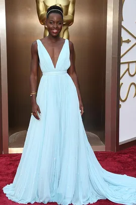 Woman in flowing light blue gown on red carpet, standing in front of a gold Oscar statue.