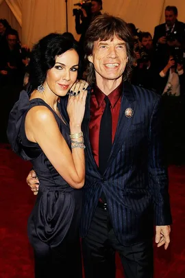 A man and woman pose together on a red carpet, both smiling and dressed in formal attire, surrounded by photographers.