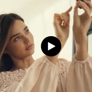 Model adjusting light while posing with calm expression, wearing a soft beige blouse, part of H&M campaign promo.