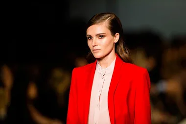 A woman in a bright red blazer and light blouse on a runway.