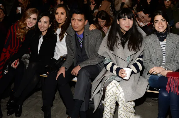 Group of six fashionable individuals sitting together at a fashion event.