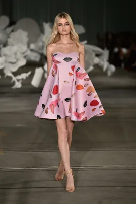 Model walks runway at Mercedes-Benz Fashion Week wearing a pink strapless dress with a lip print design.