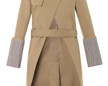 Tan long trench coat with asymmetric front, epaulets, belted waist, and patterned cuff detailing.