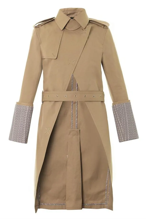 Tan long trench coat with asymmetric front, epaulets, belted waist, and patterned cuff detailing.