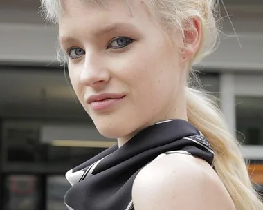 A model with a unique grey and blonde hairstyle, wearing a black and white scarf, poses with a slight smile at MBFWA.