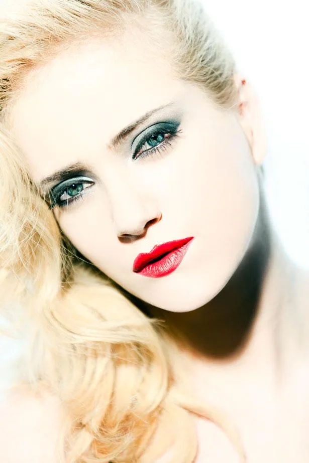Blonde woman with smoky eye makeup and red lipstick, in a close-up, high-contrast photo.