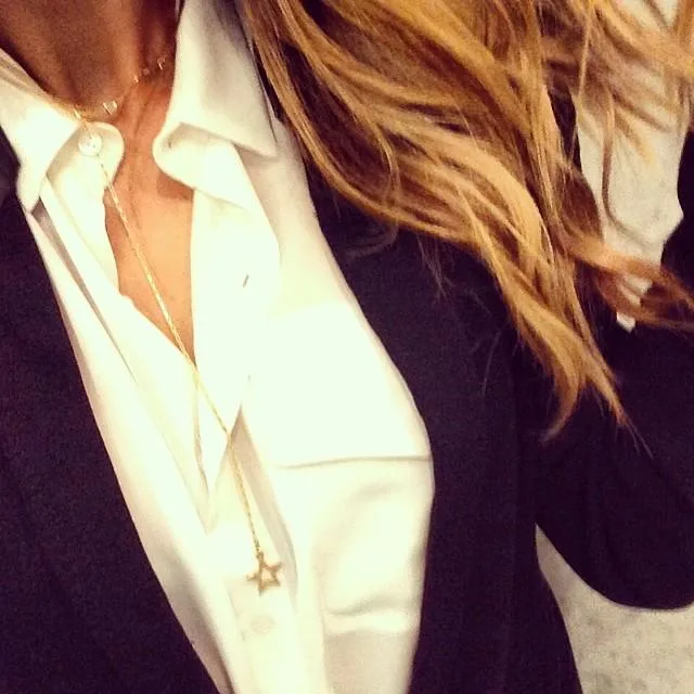 Business attire: Woman in white shirt, black blazer, star necklace, and wavy blonde hair, partial view.