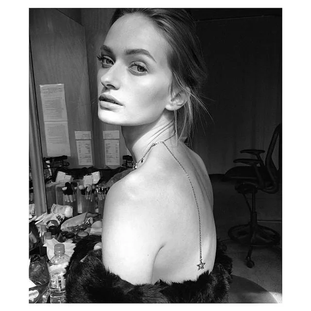 "Black and white photo of a woman in makeup room, looking over her shoulder with a star necklace on her back."