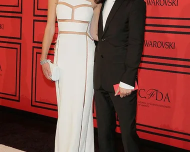 Two fashionably dressed individuals pose together on a red carpet at a CFDA event.