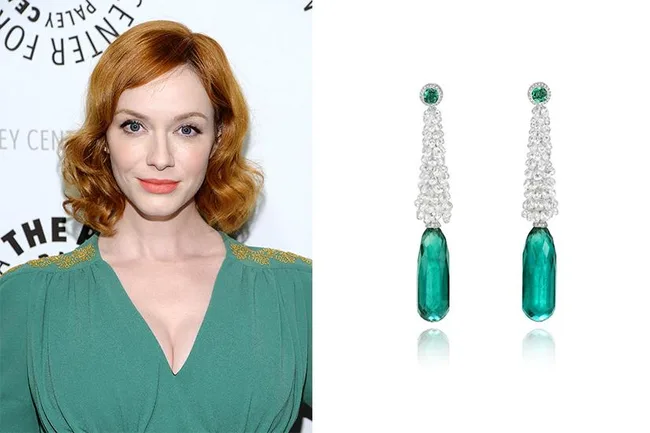 A woman with red hair in a green dress next to a pair of long, emerald and diamond earrings.