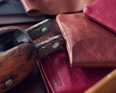 Close-up of handmade leather wallets in red and brown, with a traditional leatherworking tool placed nearby.