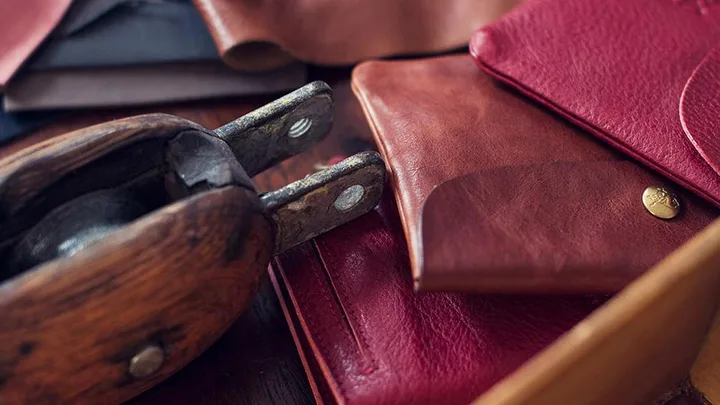 Close-up of handmade leather wallets in red and brown, with a traditional leatherworking tool placed nearby.