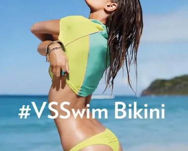 Model in a yellow bikini on a beach, displaying the hashtag #VSSwim Bikini.