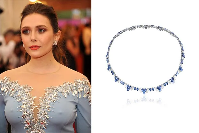 Person in a blue dress with a jeweled design, next to a blue gemstone necklace on a white background.