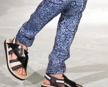 Person walking in floral-patterned trousers and black sandals on a runway.