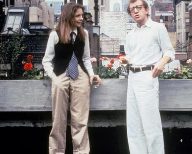 Diane Keaton as Annie Hall in a vest and tie, chatting with Woody Allen, in a rooftop garden setting.