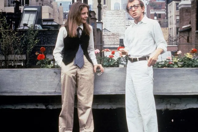 Diane Keaton as Annie Hall in a vest and tie, chatting with Woody Allen, in a rooftop garden setting.