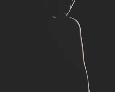 A silhouette of a person in low light with subtle contours and shadows visible against a dark background.