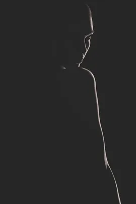 A silhouette of a person in low light with subtle contours and shadows visible against a dark background.