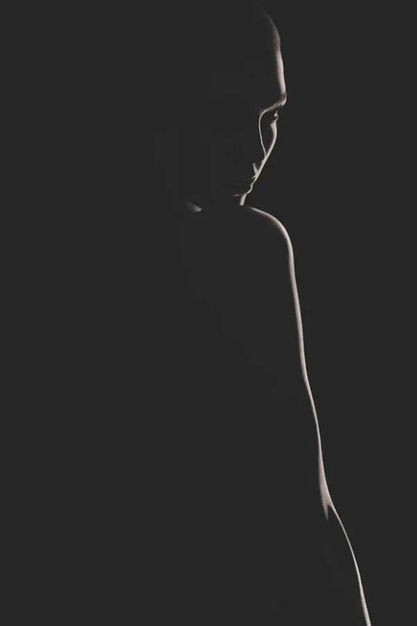 A silhouette of a person in low light with subtle contours and shadows visible against a dark background.